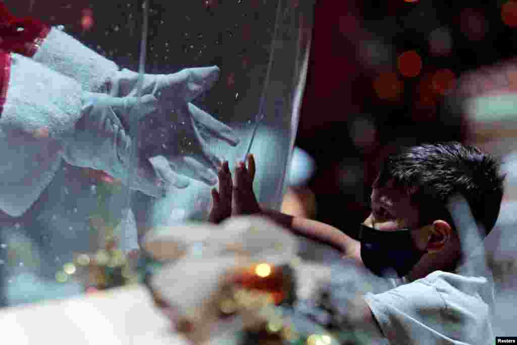 Abilio da Cruz Pinto, 77, dressed as Santa Claus inside a plastic bubble, greets a child in a shopping mall amid the COVID-19 outbreak in Brasilia, Brazil, Dec. 15, 2020.