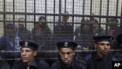 Policemen sit in front of a cage holding Egyptian employees of several pro-democracy groups during court proceedings in Cairo, Egypt, Sunday, February 26, 2012.