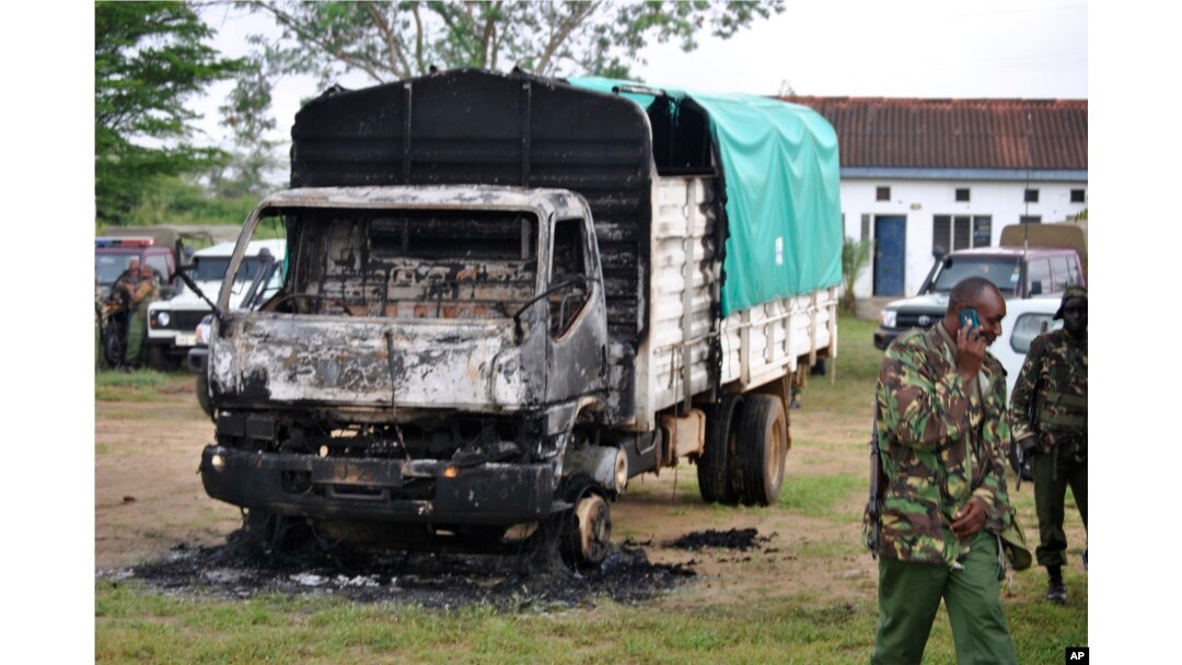 Policemen stand near the wreckage of a burnt vehicle after gunmen attacked outside Gamba police station in Gamba, Kenya, July 6, 2014.