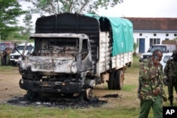 Policemen stand near the wreckage of a burnt vehicle after gunmen attacked outside Gamba police station in Gamba, Kenya, July 6, 2014.