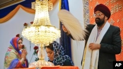 Balbir Singh Pahwa, right, of the Guru Nanak Darbar Sikh house of worship, shows respect for the holy scripture by waving a fan above Satinder Kaur, center, as she leads a prayer recital at the temple, in Hicksville, N.Y. The beards and turbans are symbols of equality in a religion that opposes India's caste system, April 9, 2017. 