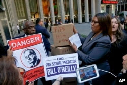 A security guard blocks an entry way as New York Public Advocate Letitia James, second from right, and protesters attempt to deliver boxes of petitions calling for the network to fire Bill O'Reilly, in New York, April 18, 2017.