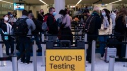 Thanksgiving holiday travelers wait in line for screening near a sign for a COVID-19 testing site at the Los Angeles International Airport in Los Angeles, Nov. 24, 2021.