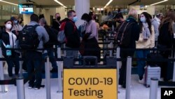 Thanksgiving holiday travelers wait in line for screening near a sign for a COVID-19 testing site at the Los Angeles International Airport in Los Angeles, Nov. 24, 2021.
