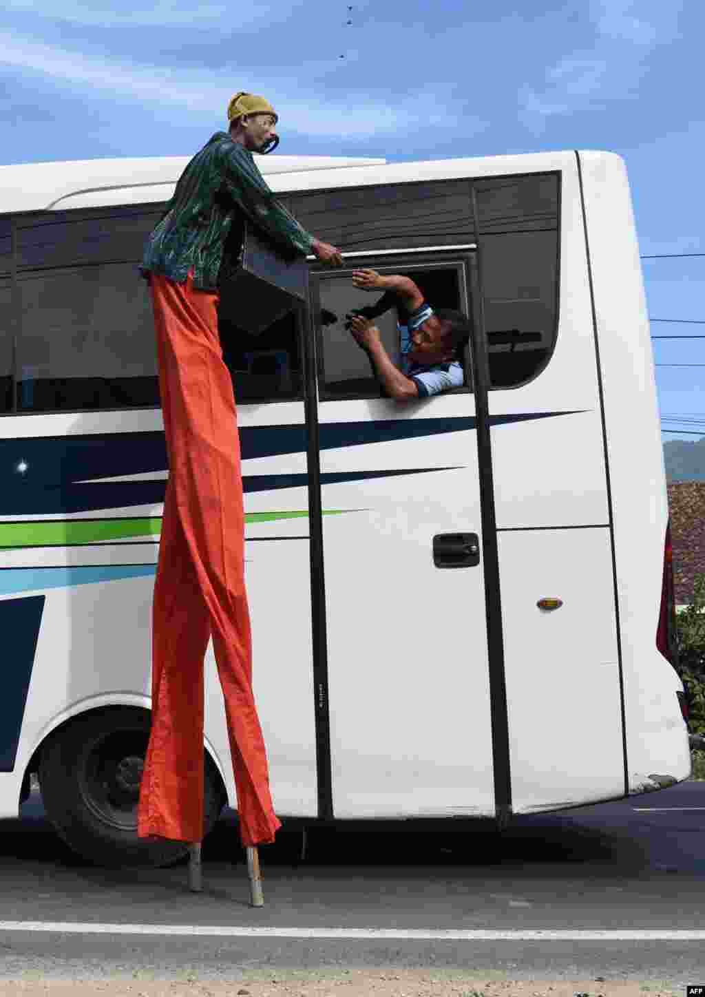 A performer on stilts receives money from a man on a bus in Garut, West Java, as Indonesians travel to their hometowns ahead of the Eid al-Fitr festival.