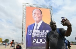 A man takes a selfie in front of Ivorian President Alassane Ouattara's campaign poster, in Abobo, a suburb of Abidjan, Oct. 16, 2020.
