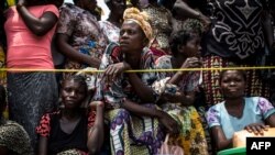 FILE - A woman looks on while people wait for their ration of food to be handed out at a food distribution Oct. 25, 2017 in Kasala, in the restive province of Kasai, Democratic Republic of Congo.