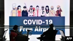 지난 17일 한국 인천국제공항에서 "COVID-19가 없는 공항"이 적힌 전광판 앞으로 마스크를 착용한 여행객들이 앉아 있다. 