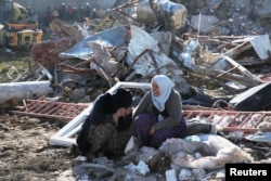 People sit in front of a collapsed building, following an earthquake in Kahramanmaras, Turkey February 7, 2023. (REUTERS/Dilara Senkaya)