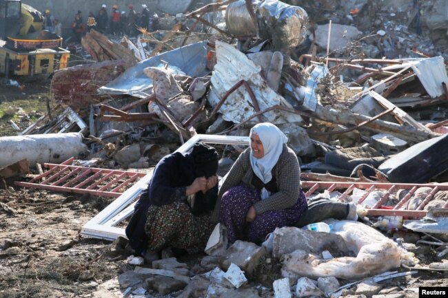 People sit in front of a collapsed building, following an earthquake in Kahramanmaras, Turkey February 7, 2023. (REUTERS/Dilara Senkaya)