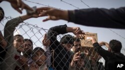 Displaced Iraqis gather by the fence to buy food and supplies from vendors standing outside the Chamakor camp, east of Mosul, Iraq, March 12, 2017.