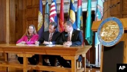 Democratic Rep. Mary Caferro, left, and Republican Rep. Ed Buttrey, right, look on as Democratic Gov. Steve Bullock signs a bill to continue Montana's Medicaid expansion program, May 9, 2019 in Helena, Mont.