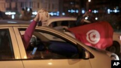 Peopel celebrate with a poster of Kais Saied and Tunisian flags in Tunis, Oct. 13, 2019. Tunisian polling agencies are forecasting that conservative law professor Kais Saied has overwhelmingly won the North African country's presidential election. 