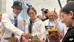 Los deportistas palestinos Yazan Al Bawwab y Valerie Tarazi toman dátiles ofrecidos por un niño a su llegada al aeropuerto de París, el jueves 25 de julio de 2024 Paris.