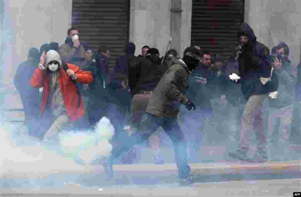 Protesters try to avoid a tear gas canister during clashes in central Athens on Wednesday, Feb. 23, 2011. Scores of youths hurled rocks and petrol bombs at riot police after clashes broke out Wednesday during a mass rally taking place as part of a genera
