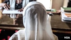 A young girl sits with her mother at the lawyer's office. She says her neighborhood sexually abused her. (C. Oduah/VOA)