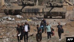 EDITORS NOTE: Graphic content / Palestinians fleeing the north along Salaheddine road help a man with a bandaged leg as they walk in front of Israeli army tanks in the Zeitoun district on the southern outskirts of Gaza City on November 24, 2023, following