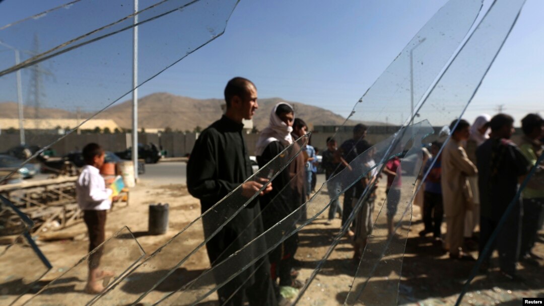 Warga di balik kaca jendela yang pecah di lokasi pemboman di luar kantor pemberantasan narkoba dekat bandara Kabul (22/7). (Reuters/Omar Sobhani)