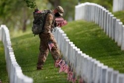 A member of the 3rd U.S. Infantry Regiment also known as The Old Guard wears a face mask as he places flags in front of each headstone for "Flags-In" at Arlington National Cemetery in Arlington, Va., May 21, 2020, ahead of Memorial Day.