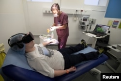 A nurse treats a patient wearing the 3-D therapeutic virtual reality headset developed by the Healthy Mind startup, at the emergency services department of the Saint-Joseph Hospital in Paris, June 7, 2018.