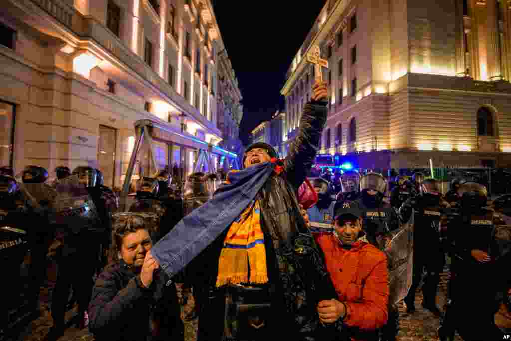 A woman screams holding a cross in front of riot policemen blocking a street following clashes with supporters of Calin Georgescu after Romania&#39;s electoral body rejected his candidacy in the presidential election rerun in Bucharest.