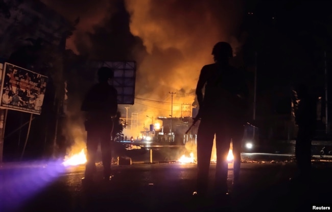 Pasukan keamanan siaga sementara sebuah gedung terbakar dalam aksi protes rusuh di Jayapura, Papua, Kamis malam (29/8). (Foto: Antara/Reuters)