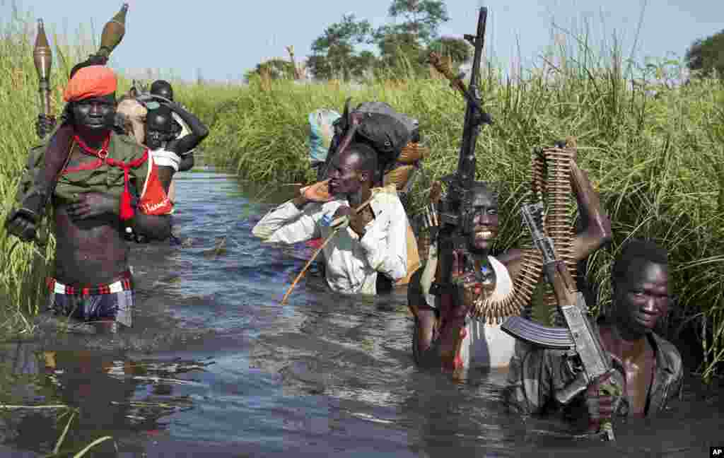 Rebel soldiers patrol and protect civilians as the civilians walk through flooded areas to reach a makeshift camp for the displaced situated in the United Nations Mission in South Sudan (UNMISS) base in the town of Bentiu, South