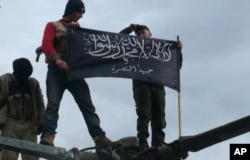 FILE - Rebels from al-Qaida-affiliated Jabhat al-Nusra, also known as the Nusra Front, wave their brigade flag, as they step on the top of a Syrian air force helicopter at Taftanaz air base that was captured by the rebels in Idlib province, northern Syria, Jan. 11, 2013.