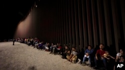 ARCHIVO - Migrantes esperan junto a un muro fronterizo el 23 de agosto de 2022, después de cruzar desde México cerca de Yuma, Arizona.