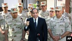 In this photo provided by MENA news agency, Egyptian President Abdel Fattah el-Sissi speaks in front of the state-run TV ahead of a military funeral for troops killed in an assault in the Sinai Peninsula, as he stands with army commanders in Cairo, Oct. 25, 2014.