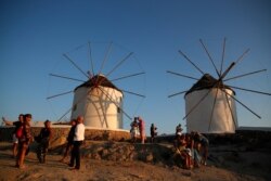 FILE - People gather as the sun sets at the windmills on the Aegean Sea island of Mykonos, Greece, Aug. 16, 2020.