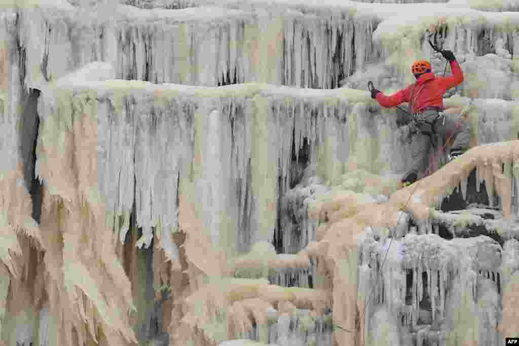 An ice climber ascends Kinder Downfall, a frozen waterfall in the Peak District National Park, near Hayfield, northwest England, as snow blankets the region.