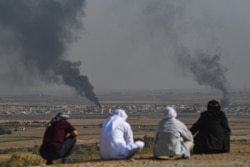 People look on as smoke rises from the Syrian town of Ras al-Ain, in a picture taken from the Turkish side of the border in Ceylanpinar, Oct. 11, 2019.