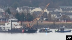 A member of a dive team and a Coast Guard vessel with a crane are pictured as they work near the wreckage of a Black Hawk helicopter in the Potomac River from Ronald Reagan Washington National Airport, Jan. 31, 2025, in Arlington, Va. 