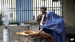 An Afghan woman clad in burqa buys a broom along a roadside in Kabul June 13, 2011.
