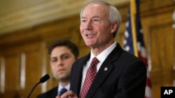 Arkansas Gov. Asa Hutchinson answers reporters' questions as Sen. Jonathan Dismang, R-Beebe, background, listens at the state Capitol in Little Rock, Ark., Wednesday, April 1, 2015.