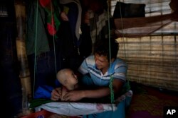 In this Jan. 21, 2018 photo, Rohingya Muslim refugee Noor Kadir, 24, from the Myanmar village of Gu Dar Pyin, plays with his son inside the family makeshift shelter in Balukhali refugee camp, Bangladesh.
