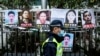 FILE - A police officer walks past placards of detained rights activists taped on the fence of the Chinese liaison office in Hong Kong, Feb. 19, 2020.