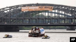 Activists of the refugee support group SeaWatch attach a poster that reads "Build bridges not walls" to a bridge over the river Elbe in Hamburg, Germany, June 28, 2017. Hamburg will host a G-20 summit July 7-8. 