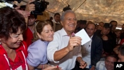 Presidential candidate Salvador Sanchez Ceren, who is also the current VP for the ruling Farabundo Marti National Liberation Front (FMLN), center, accompanied by his wife, center left, raises his ballot before casting it, El Salvador, March 9, 2014.