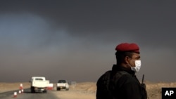 A member of the Iraqi special forces guards a checkpoint near Awsaja, Iraq, as smoke from fires lit by IS militants at oil wells and a sulfur plant fill the air, Oct. 22, 2016. There are worries coalition forces would be ill-prepared for a chemical attack.