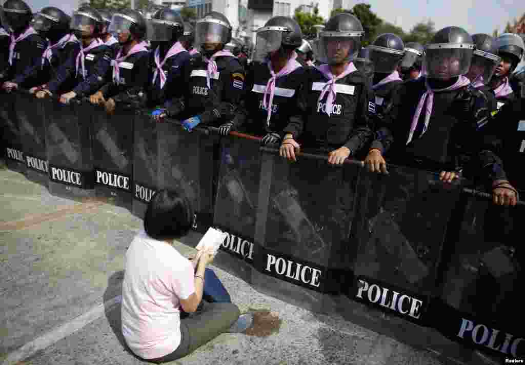 An anti-government protester sits on the ground praying in front of a line of Thai police near Government House in Bangkok, Feb. 14, 2014.