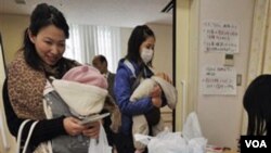 Para ibu menerima pembagian botol air di Tokyo, Kamis (24/3).