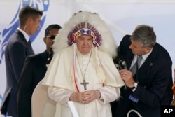 프란치스코(가운데) 교황이 25일 캐나다 북부 앨버타주 원주민 기숙학교 부지를 방문해, 원주민들이 선물한 깃털 머리장식을 쓰고 있다.