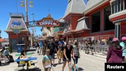 FILE - People, mostly maskless, walk past the Giant Dipper rollercoaster ride at the Santa Cruz Beach Boardwalk, in Santa Cruz, California, June 28, 2021. 