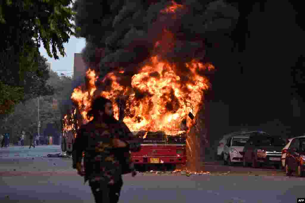 A man walks on a street as a bus is on fire following a demonstration against the Indian government&#39;s Citizenship Amendment Bill (CAB) in New Delhi.