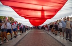 Para peserta aksi solidaritas bersama rakyat Belarus, membawa bendera Belarusia bersejarah berukuran raksasa, saat turun ke jalanan di Bialystok, Polandia, 20 Agustus 2020.