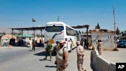 This photo released by the Syrian official news agency SANA, shows Syrian government forces overseeing the evacuation by bus of Army of Islam fighters from the besieged town of Douma, just east of Damascus, Syria, Apr. 2, 2018. 