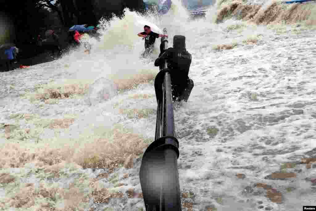 중국 저장성 항저우의 첸탄강에서 태풍 두쥐안의 영향으로 높은 파도가 치고 있다. 한 경찰이 철책에 매달린 채 물을 피하는 관광객들을 지켜보고 있다.