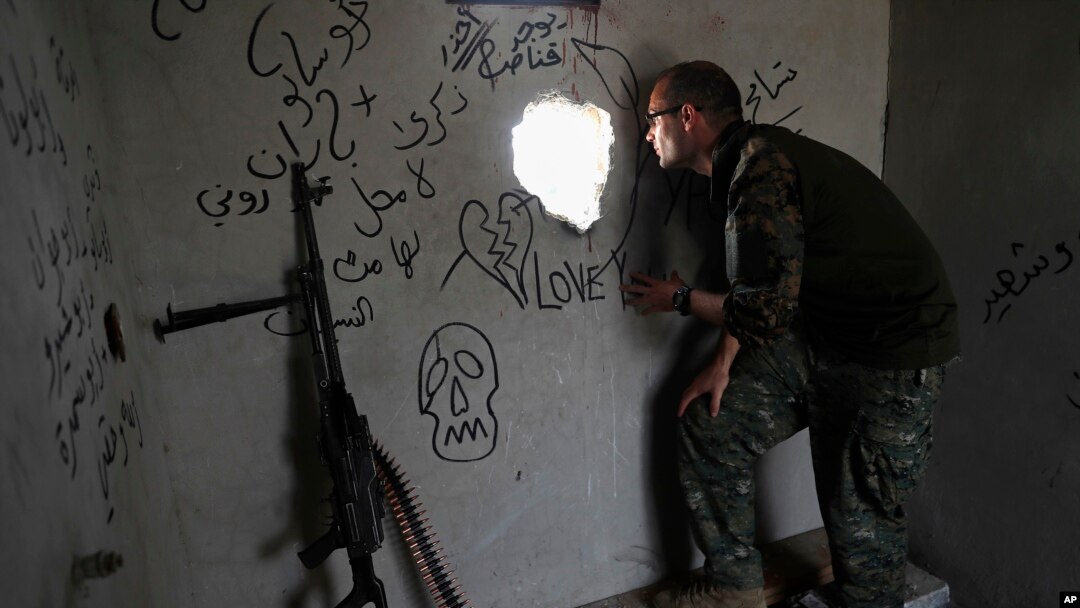 Macer Gifford, a 30-year former City broker in London, who fights with an Assyrian militia, that is part of the U.S-backed forces battling Islamic State group militants, looks through a hole into a street controlled by the IS, on the western side of Raqqa, northeast Syria, July 17, 2017.